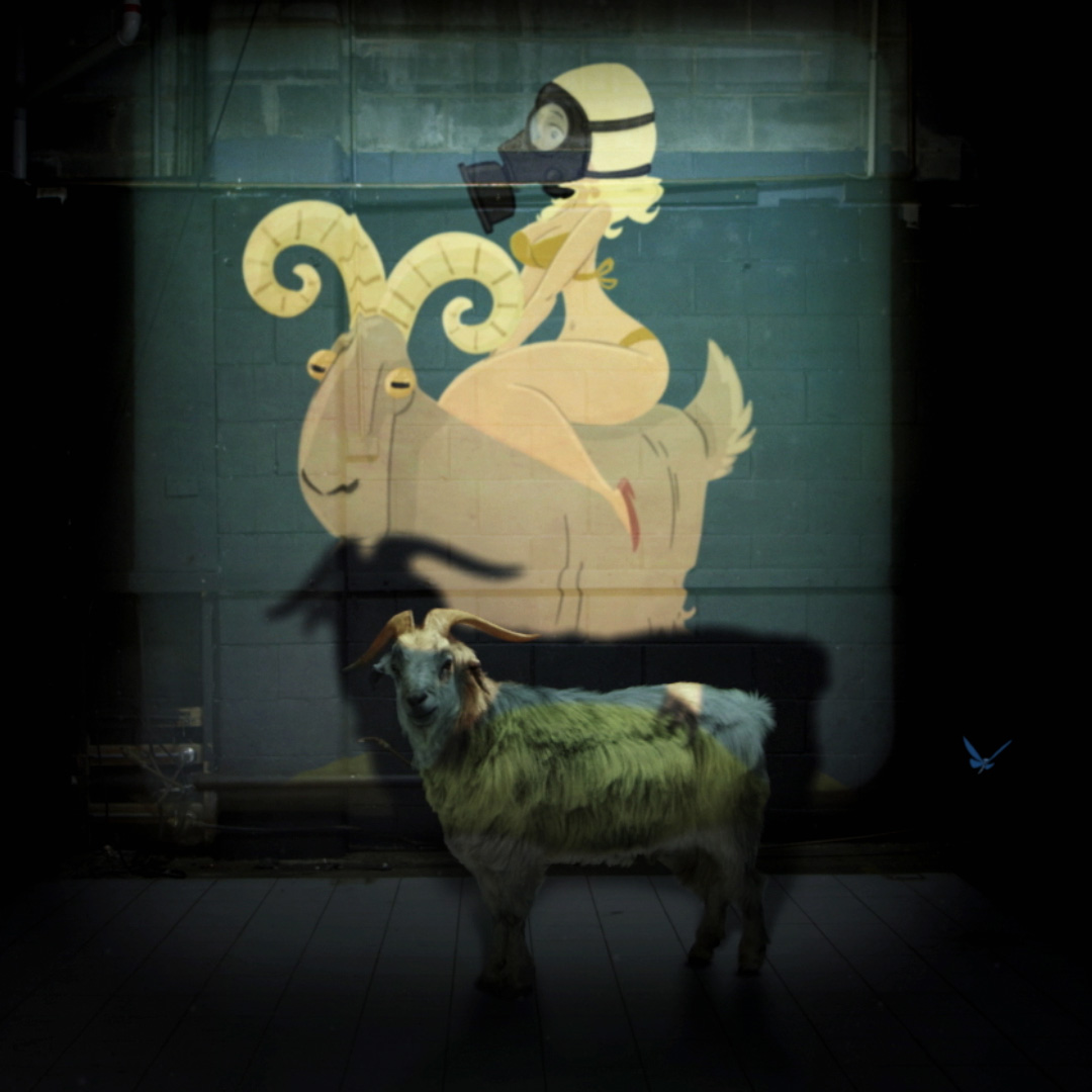 Photograph of a real goat, with an illustration of a woman in a gold bikini and gas mask sitting on its back projected over the real goat.