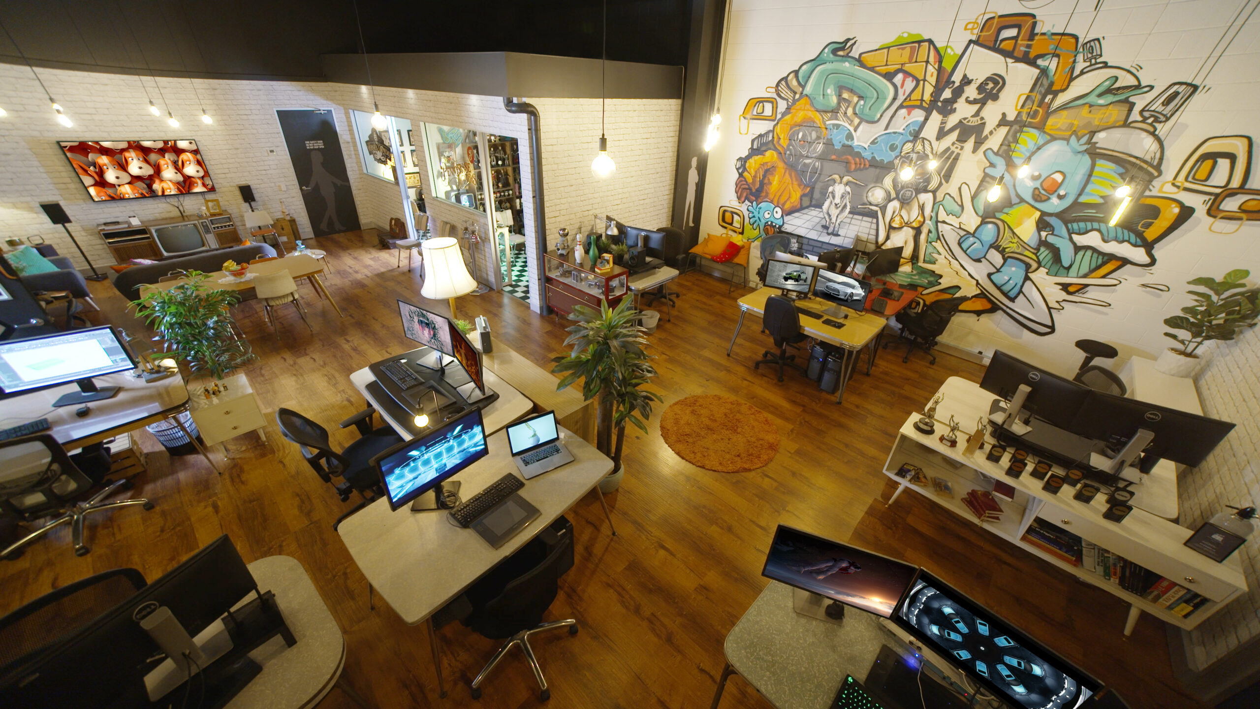 A high-angle photo of the SQUEAK studio room. There is a graffiti mural on the wall showing past projects and character designs. The room is decorated with a 1970's vibe.